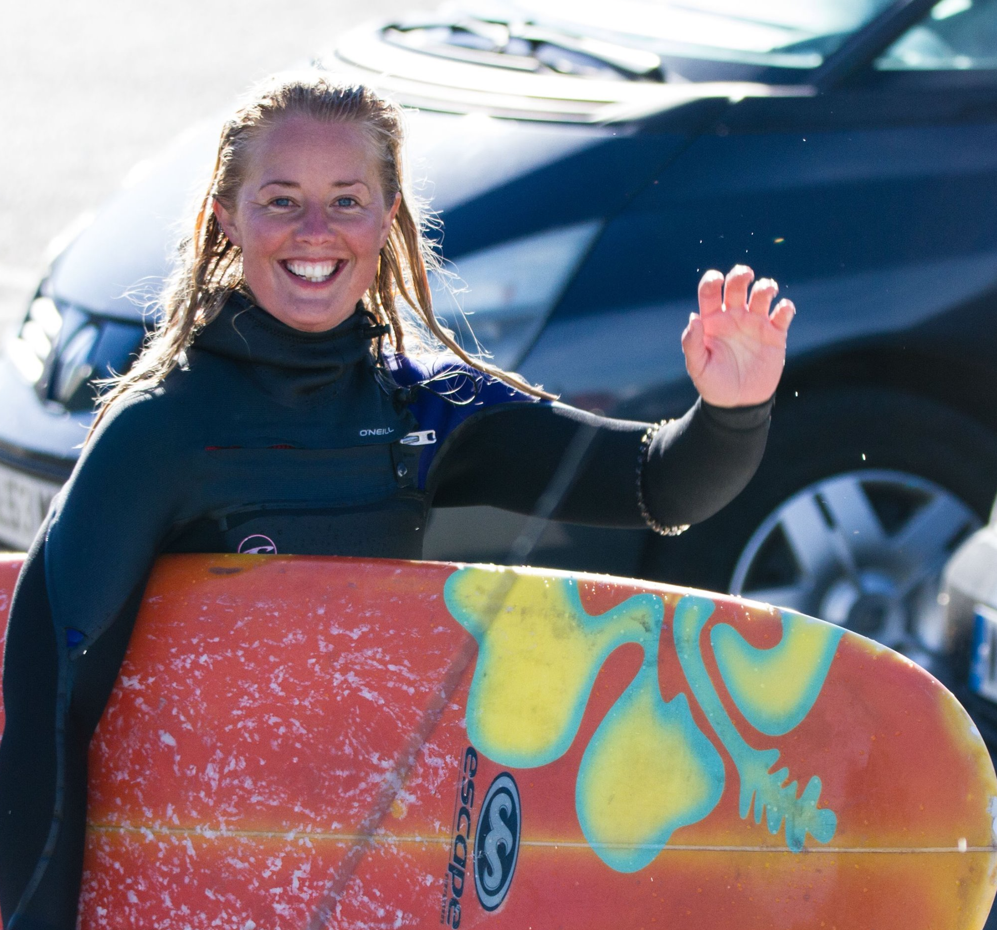 Female in wetsuit holding orange board with a yellow flower on it