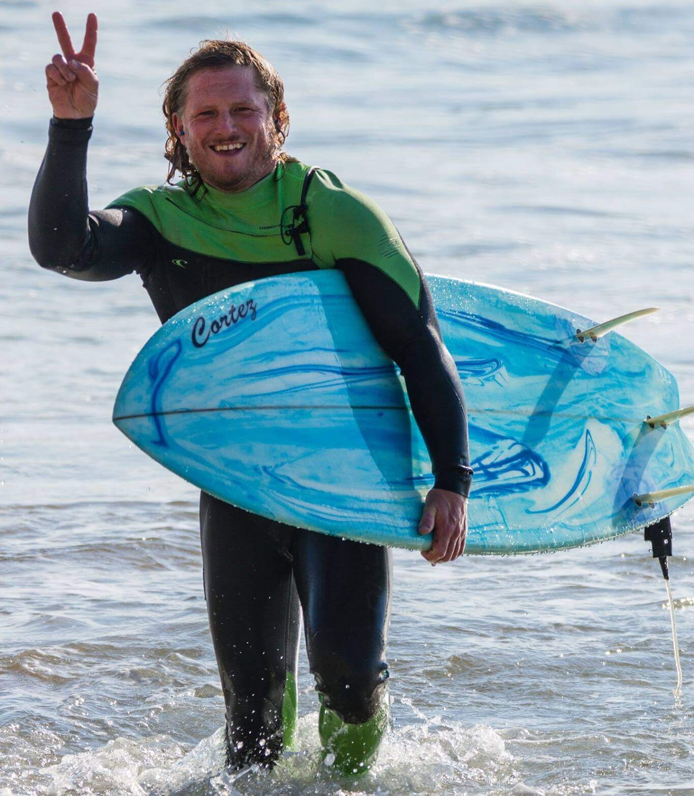 Man standing in water in wetsuit with blue surf board